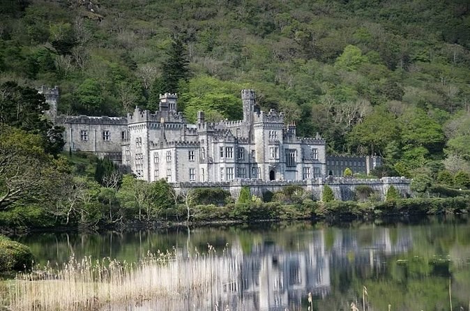 Kylemore Abbey across reeds and still water at the foot of a wooded mountain
