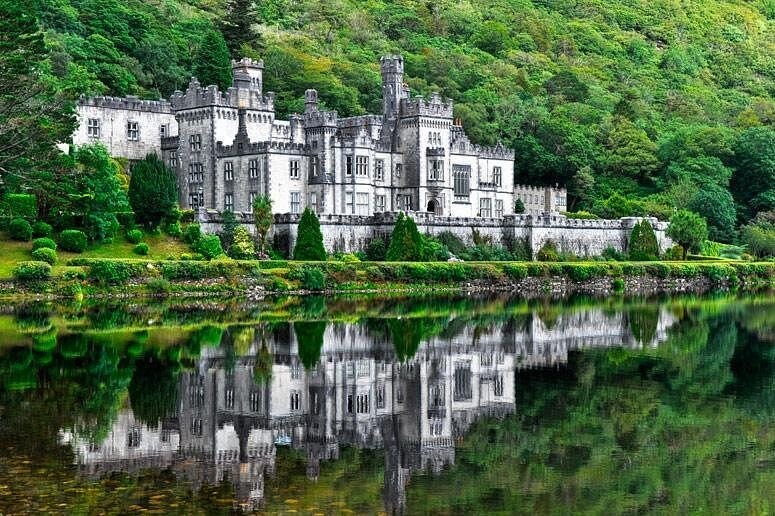 Kylemore Abbey and its reflection in the still water of the lough, below a wooded mountainside