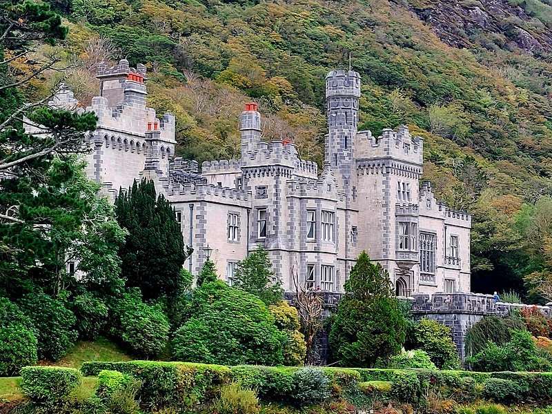 The granite towers of Kylemore Abbey above clipped shrubs and a wooded slope