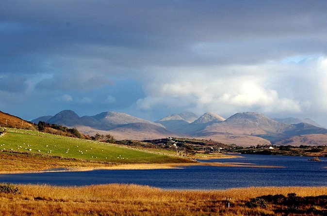 A range of bare mountains above a long lough, with autumn bog grass along the shore