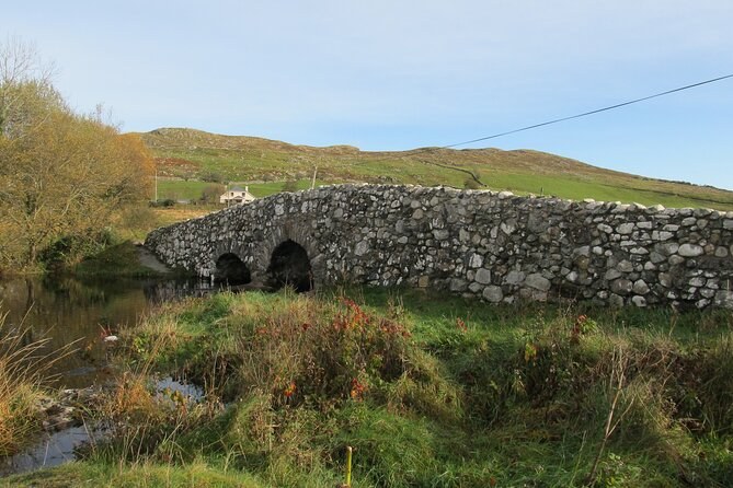 An old stone bridge of several arches over a stream in rough autumn moorland