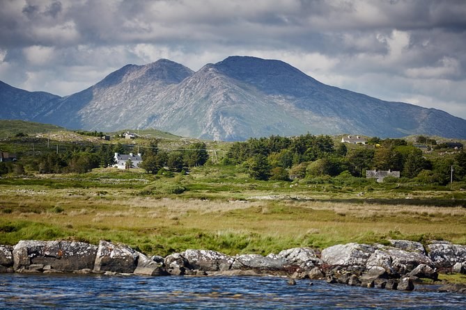 A twin-peaked mountain above bogland and white cottages, seen across a rocky shore